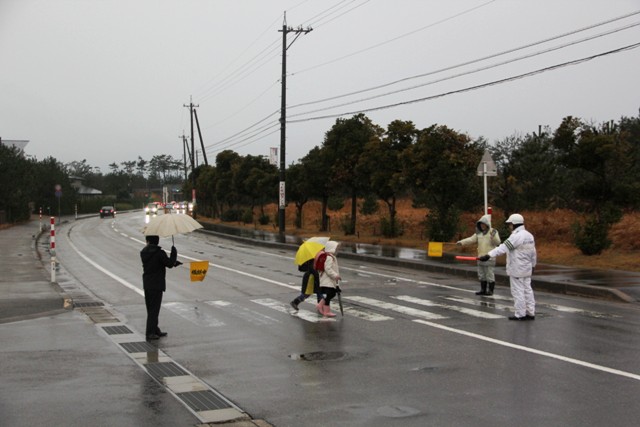 2人の子供が横断歩道を渡るのを見守るボランティアの写真