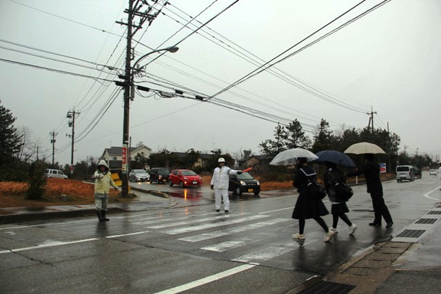 3人が横断歩道を渡るのを見守るボランティアの写真