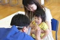 コスモアイル羽咋で母親に抱っこされた子どもが歯科医師に歯を診てもらっている写真