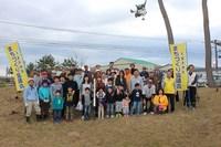 黄色の旗を持った千里浜地区まちづくり協議会の方たちと参加した親子が記念撮影している写真