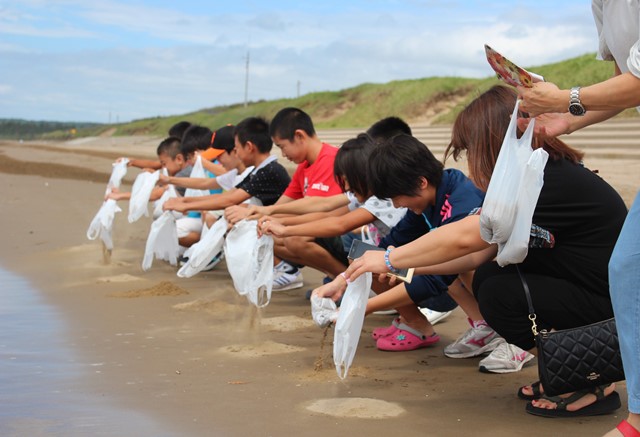 千里浜海岸の再生を願って砂をまく参加者